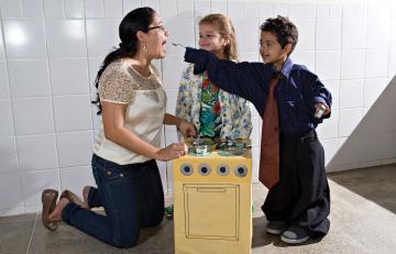Crianças brincam de faz de conta com professora e fogão