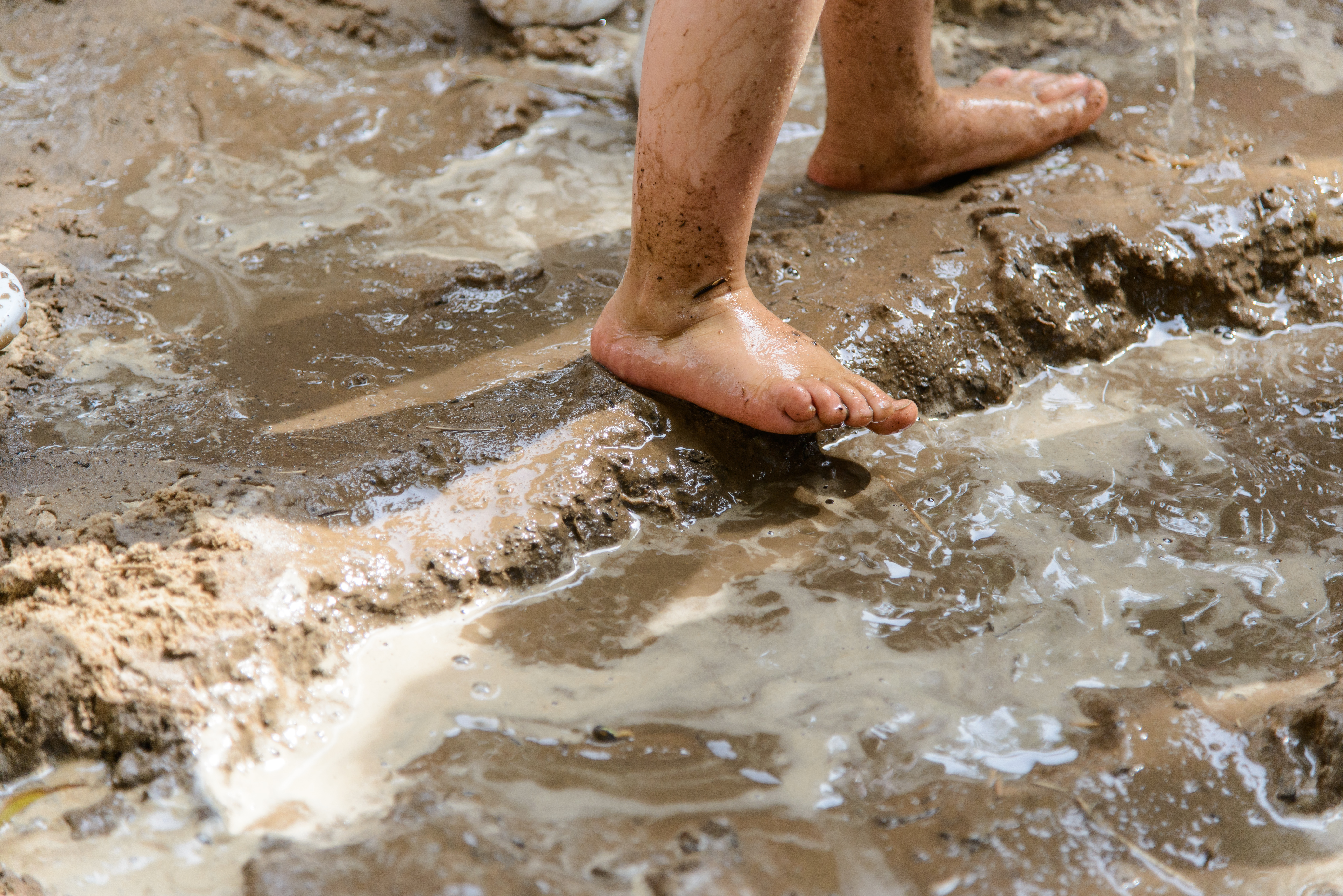 Close de pés de crianças brincando em uma poça de lama