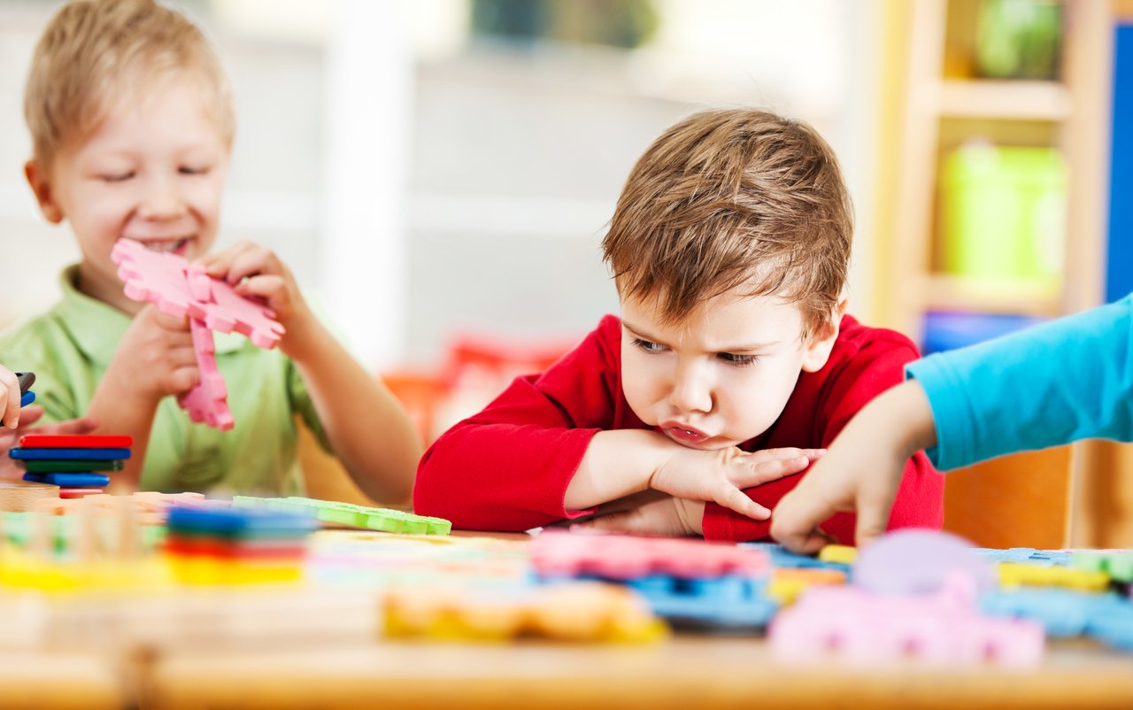 Alunos brincam em sala de aula com brinquedos coloridos em volta de um aluno com cara de bravo