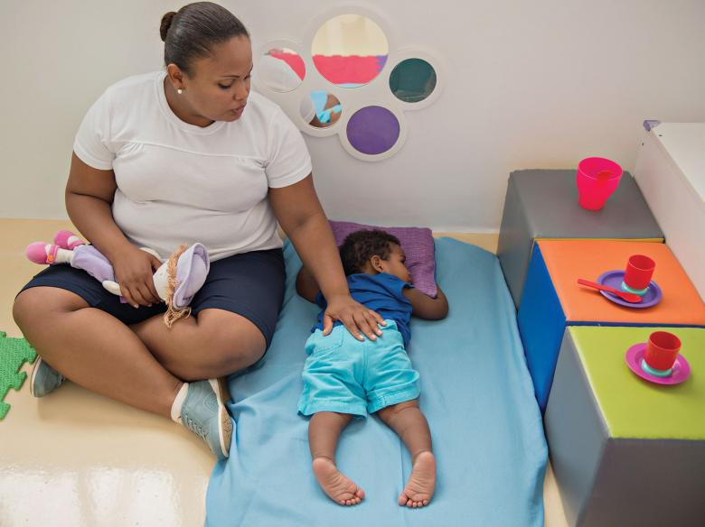 ELIANE, berçarista da Creche Ceduc, faz carinho em menino deitado no colchonete