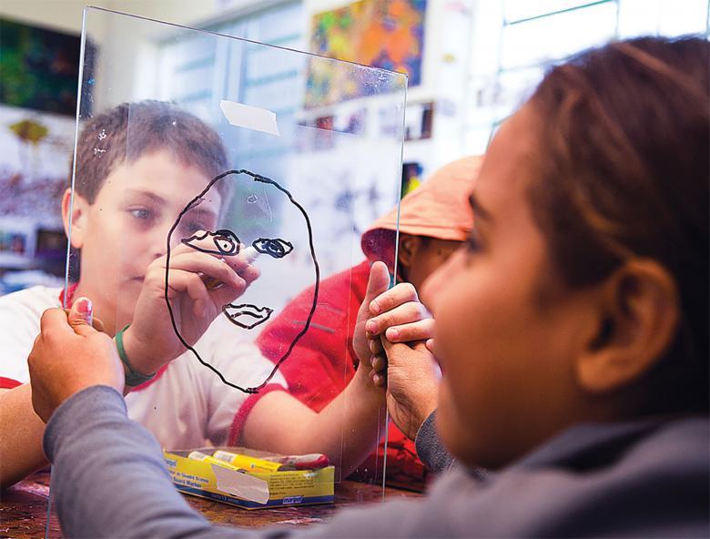 No acetato e no vidro, alunos desenham o contorno do rosto do colega