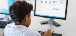 Aluno de sentado de costas olha para um computador