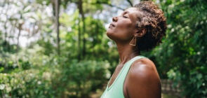 Professora olha para cima, com os olhos fechados. Ela tem uma feição relaxada. Está ao ar livre