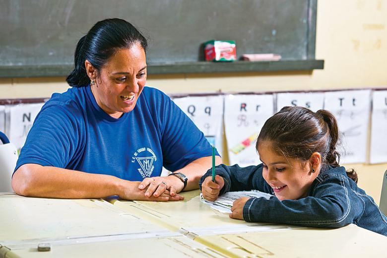 A pequena Mariana escreve com a ajuda da professora Mara