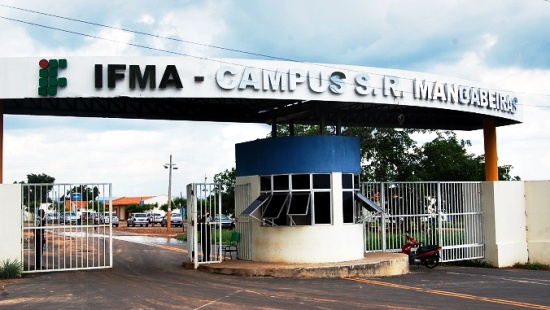 Dois portões brancos com uma guarita de janelas de vidro no meio deles, protegidos por uma laje em que se lê "IFMA - Campus S. R. Mangabeiras"