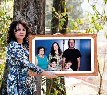 Coordenadora da escola de São Paulo segura um quadro com uma foto de uma família formada por pai, filho, irmã, sobrinha e mãe