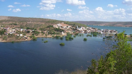 No centro da imagem, um largo rio com uma pequena cidade à sua margem e montanhas ao fundo.