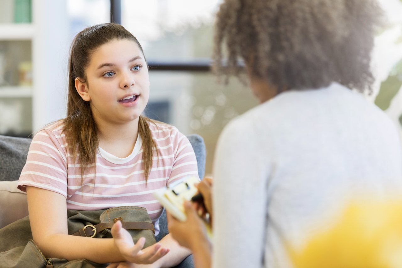Adolescente conversa com adulto em sala fechada