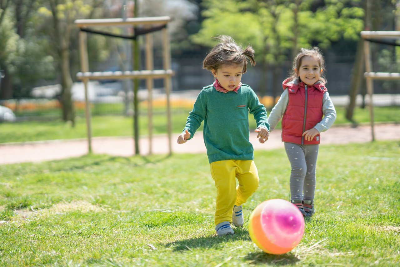 Duas meninas chutam bola colorida em um gramado de um parque